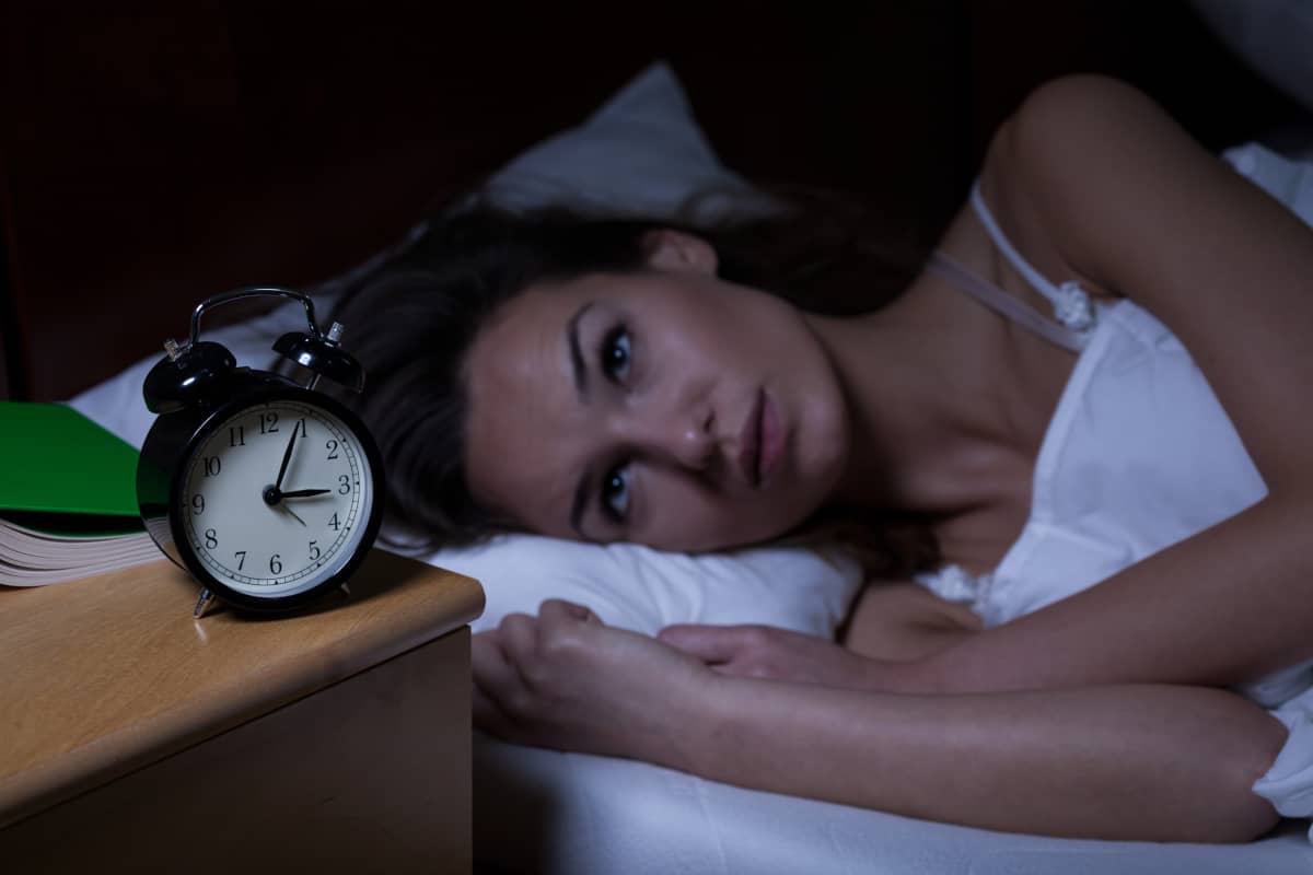 femeie care sufera de insomnie treaza noaptea in pat