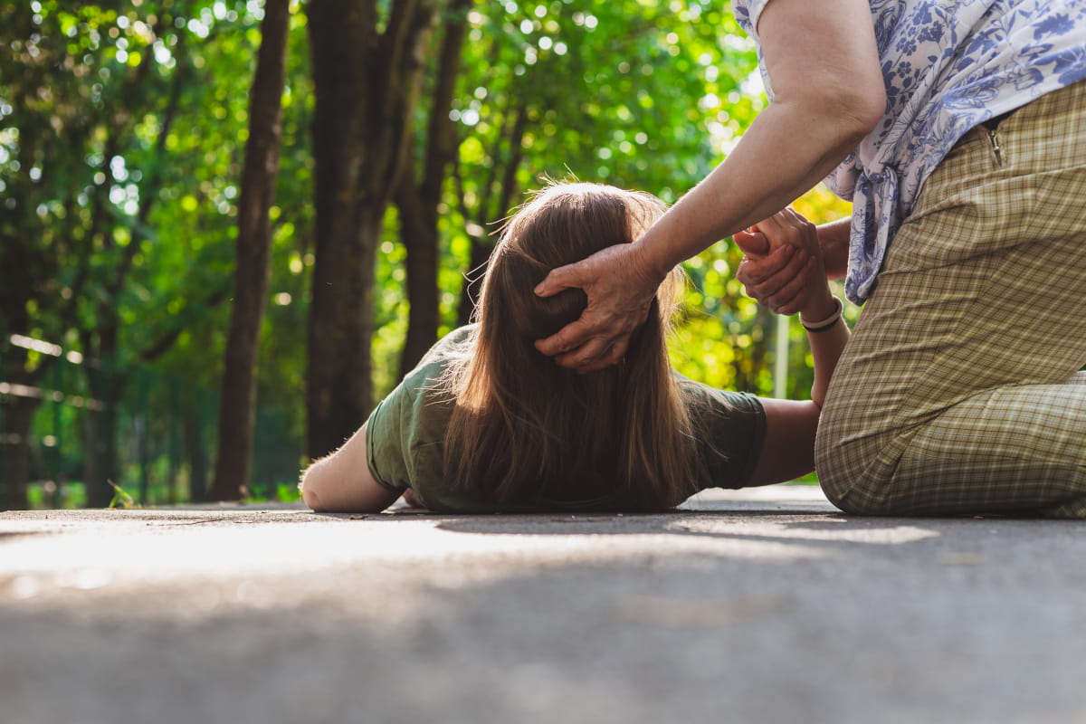 femeie varstnica sustine capul unei tinere care s-a prabusit pe asfalt in timpul unei crize de epilepsie